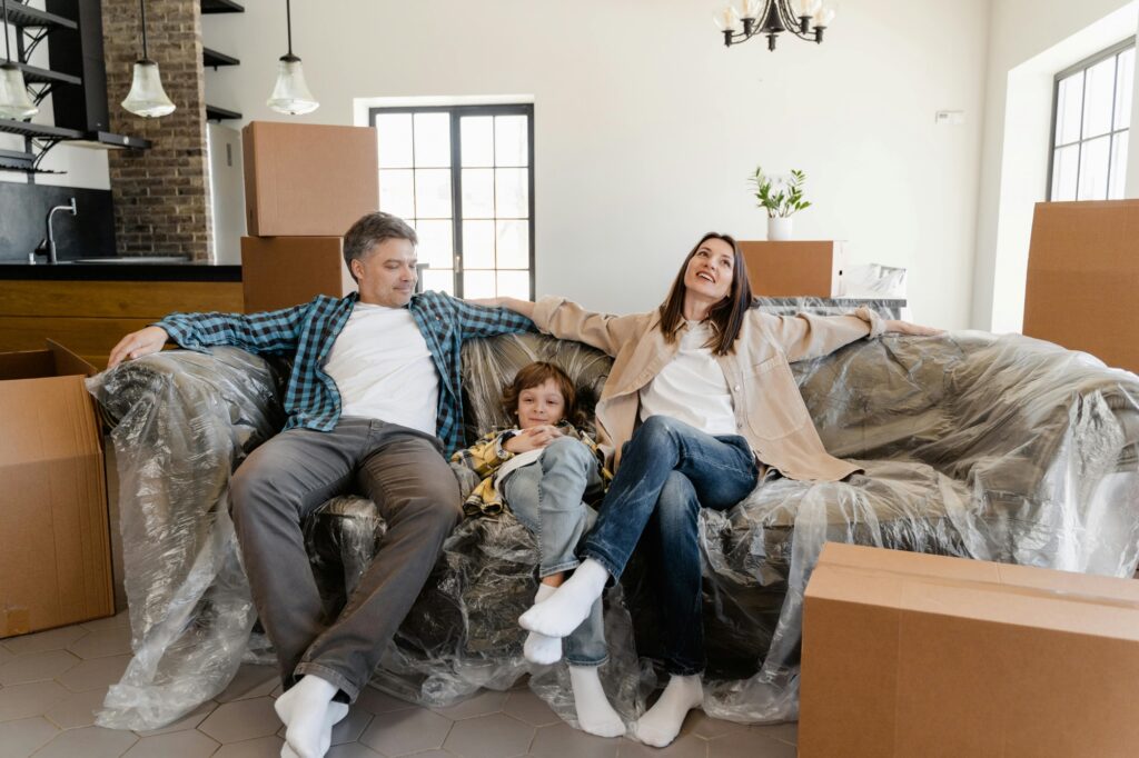 A young family is relaxing on a wrapped sofa and is surrounded by cartons after moving in.