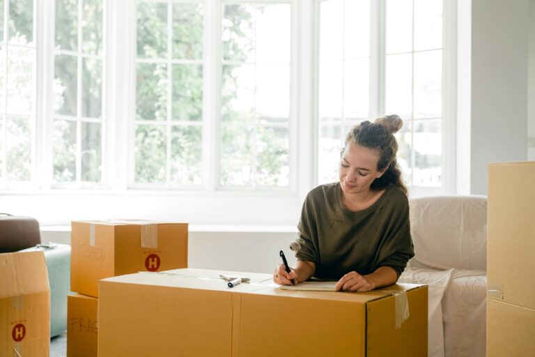 A woman is budgeting for the move and is surrounded by boxes in the concept of 'how to save money when moving to Surbiton'.