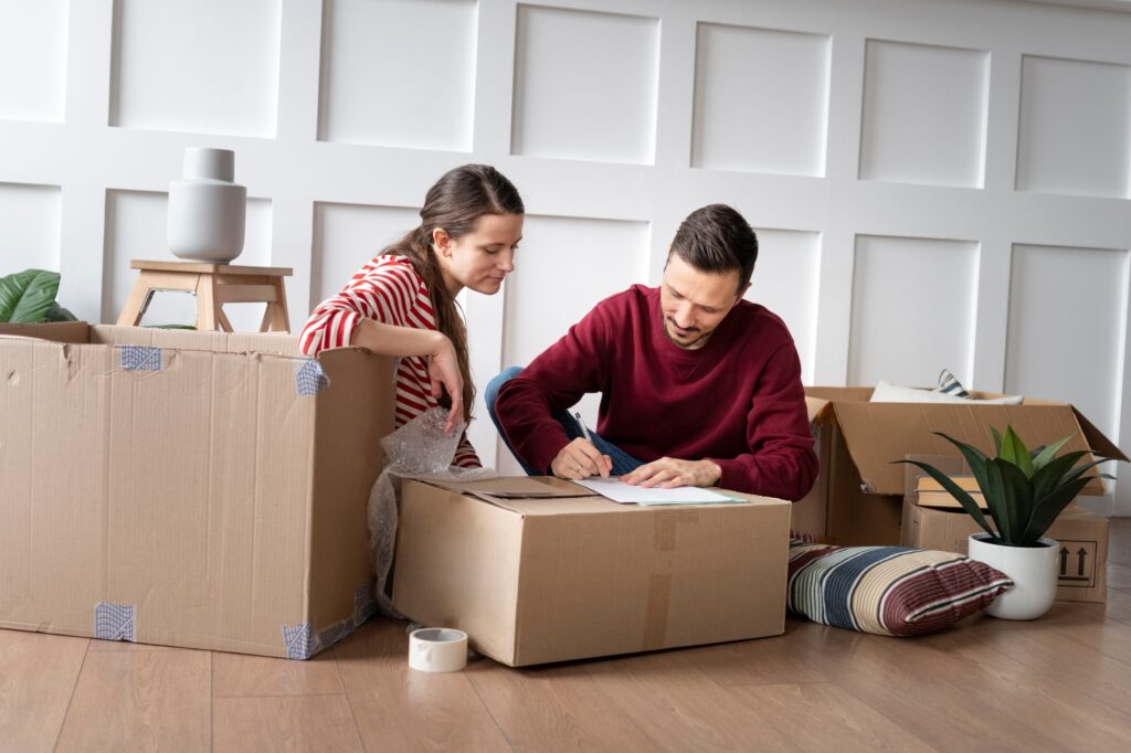 A young couple with a checklist and surrounded by packing supplies in the concept of 'Moving to Surbiton: Understanding the Differences Between Man and Van and Traditional Removals'.