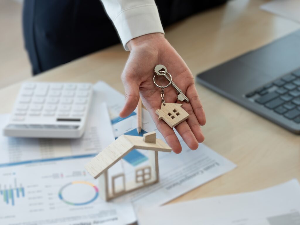 A house-shaped keychain on a man's hand and calculator and laptop on the background in the concept of comparing man and van quotes when moving in Surbiton